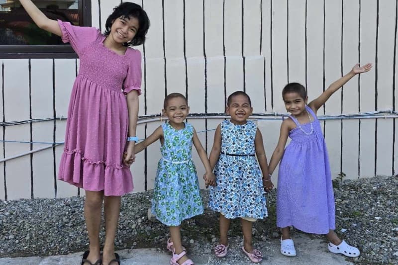 Four girls hold hands and smile outside the Everlasting Hope home.