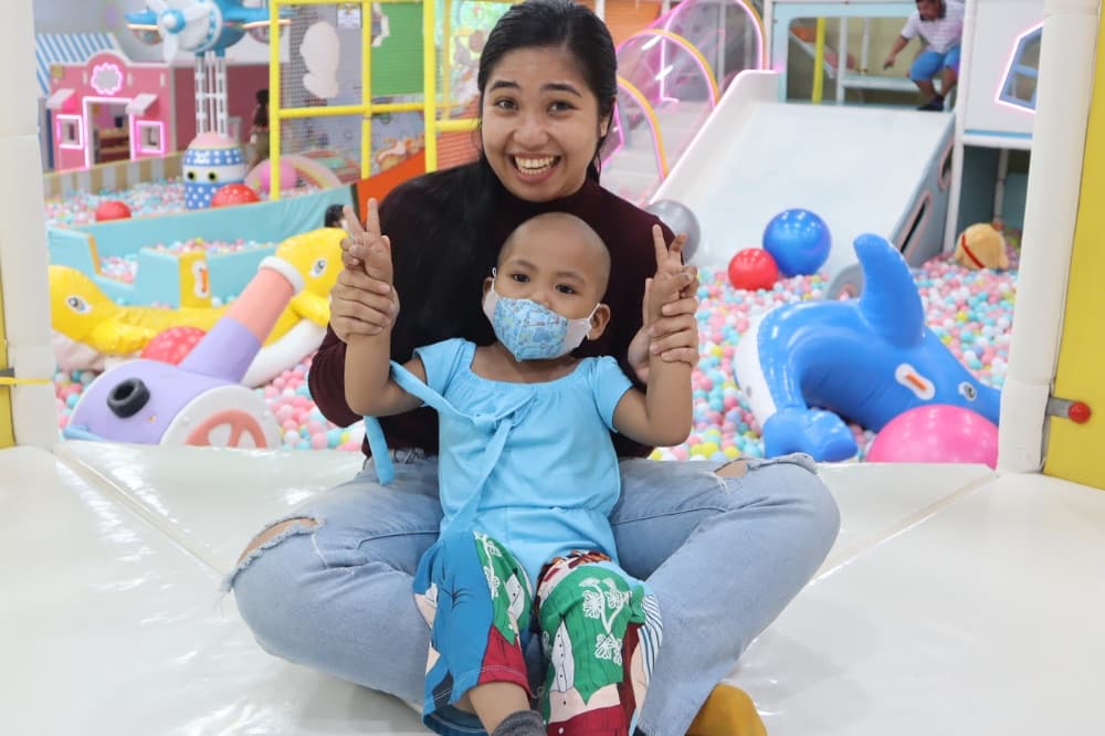 Gresamae smiles with a caregiver in a colorful play area.