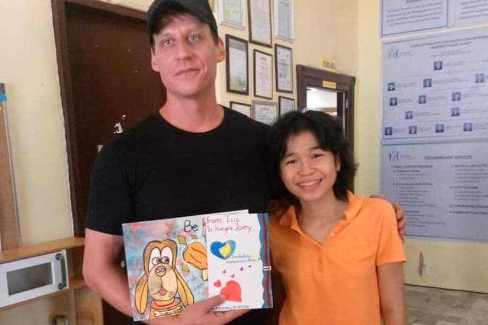 Joey Smitherman stands beside a child holding a handmade card.